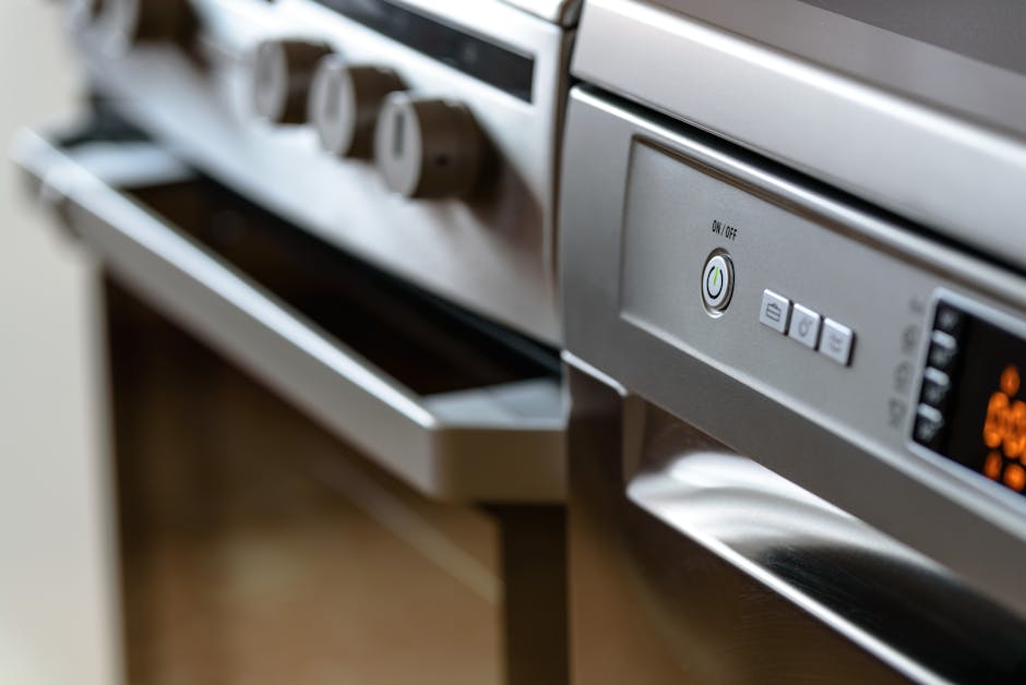 A person wearing yellow and blue rubber gloves is cleaning the stovetop of a white gas cooktop with a blue cloth, removing grease and food stains from the ceramic surface. The cooktop has two burners,